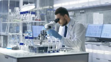 Araştırma bilim adamı görünüyor içine mikroskop ve gözlemler aşağı yazıyor. Modern laboratuvar birinde yürüten deneyler olduğunu.