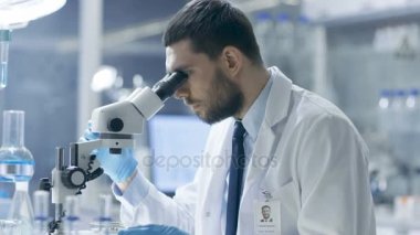 Araştırma bilim adamı görünüyor içine mikroskop ve gözlemlerini aşağı yazıyor. Modern bir laboratuarda çalışıyor.