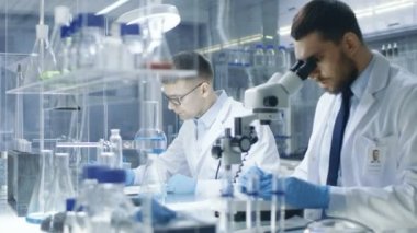 Modern bir laboratuarda iki bilim adamları deneyler. Baş araştırma bilim asistanı için mikroskop içinde gördüğü sonuçları belirler.