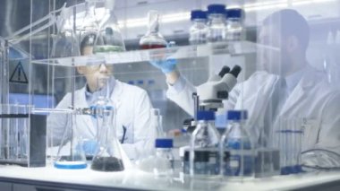 Bir Modern laboratuvar araştırma bilim adamı alır ölçek raf ve görünüyor içine kimyasal madde ile mikroskop içine bileşik olduğunu. Meslektaşı dikkatle aşağı her adım yazıyor.