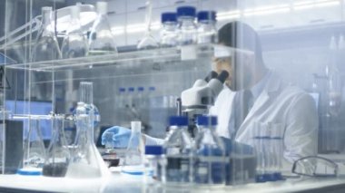 Modern laboratuvar bilim adamı kabı içindeki karanlık sıvı ile inceler sonra gelirleri ile mikroskop kullanarak. 