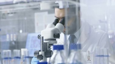 Araştırma bilim adamı görünüyor içine mikroskop ve gözlemlerini aşağı yazıyor. Modern bir laboratuarda çalışıyor.