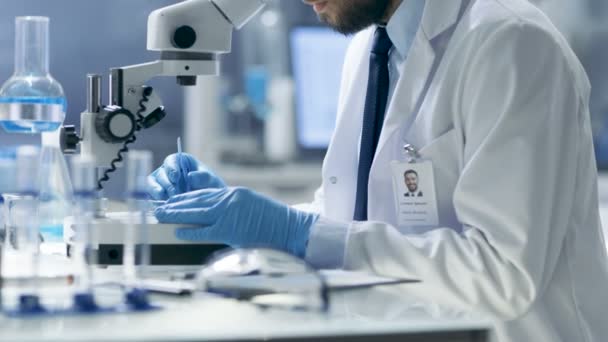 Forskning forskare justerar prov i en petriskål med kirurgiska tänger och ser på det i Mikroskop. Han arbetar i moderna laboratorier. — Stockvideo