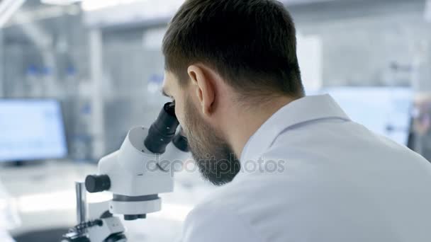 Over the Shoulder View of a Research Scientist Looking into Microscope (en inglés). Lleva a cabo experimentos con sus colegas en el laboratorio moderno . — Vídeo de stock