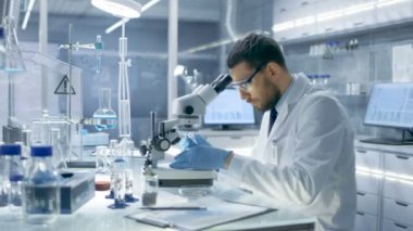 Modern bir Laboaratory araştırma bilim adamı kullandığı pipet damla madde bir kaydırıcı ve Examines bu mikroskop altında. O sonra gözlemlerini yazıyor.