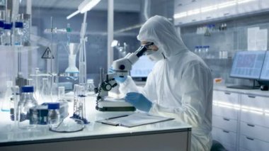 Güvenli bir yüksek düzey araştırma laboratuvarı bilim adamı bu durumda bir Coverall Petri kabına mikroskop altında inceler..