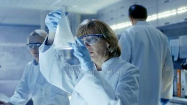 Üst düzey kadın kimyacı Ultra Modern laboratuvar sıvı kimyasallar ile çalışır. O bilgisayarlardaki verilerin analiz onun meslektaşları ve onlar Her masada oturur.