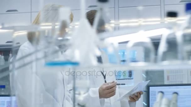 Female and Male Chief Scientists Walking Through Modern Laboratory and Discussing Future Possibilities. Young Woman Assistant Works on Computer at Her Desk. — Stock Video