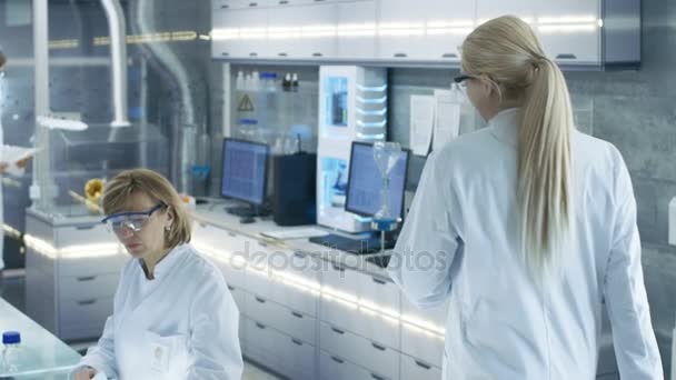 Follow-up Shot van jonge laboratorium-assistent wandelen met haar werkplek. Mannelijke en vrouwelijke wetenschappers van verschillende leeftijd werken in dit laboratorium State of the Art. — Stockvideo