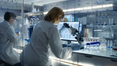 Üst düzey kadın biyolog çalışır onun bilgisayar ve malzemeleri mikroskop altında bakar. Modern bir laboratuvarda bir kız.