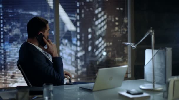 Empresario sentado en su escritorio hablando por teléfono en su oficina con Big City View . — Vídeos de Stock