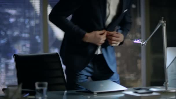 El hombre de negocios desabrocha su chaqueta y se sienta en su escritorio, comienza a escribir en su computadora portátil. Su oficina tiene vista a la ventana de la gran ciudad . — Vídeo de stock