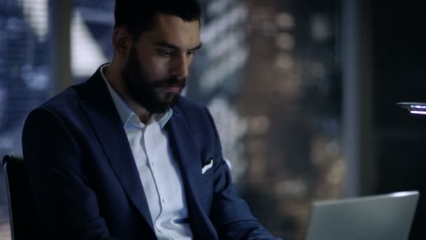 Поздно ночью бизнесмен работает над ноутбуком в своем личном кабинете с видом на окно большого города . — стоковое видео
