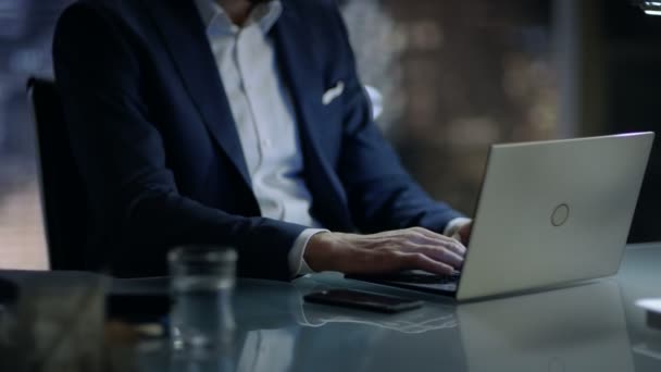 Tarde en la noche empresario trabaja en un ordenador portátil en su oficina privada con gran ciudad de la ventana. — Vídeos de Stock