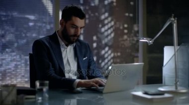 Gece geç saatlerde iş adamı büyük şehir pencere manzaralı özel ofisinde bir dizüstü bilgisayarda çalışır.