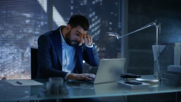 Empresário sobrecarregado Tarde da noite sente-se sonolento, mas continua trabalhando em um laptop em seu escritório privado . — Vídeo de Stock