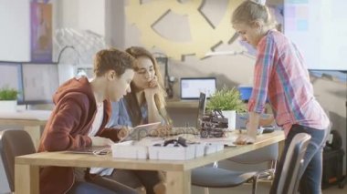 İki kız ve bir erkek bilim sınıf Robotik proje üzerinde çalışmak. Masanın üzerine çeşitli ayrıntılar, Taslaklar ve dizüstü bilgisayar var.