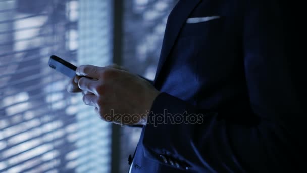 Late at Night Businessman Stands at the Window of His Private Office and Uses Smartphone. — Stock Video