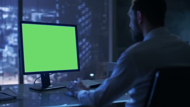 A tarda notte Businessman lavora su un personal computer con schermo verde Mock-up nel suo ufficio privato con vista Big City Window . — Video Stock