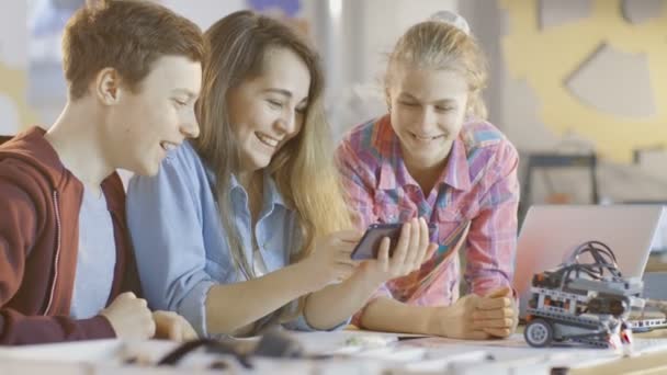 Chłopiec i dwóch dziewczyn pracujących w projekcie klasy szkoły nauki oglądać popularne filmy na smartfonie. — Wideo stockowe