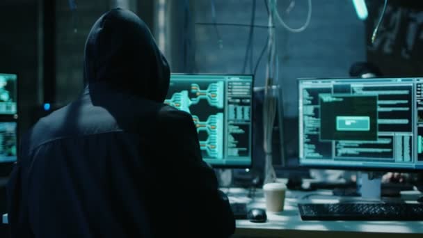 Hooded Hacker Breaks into Corporate Data Servers and Infects them with Virus. His Hideout Place has Dark Atmosphere, Multiple Displays, Cables Everywhere. — Stock Video