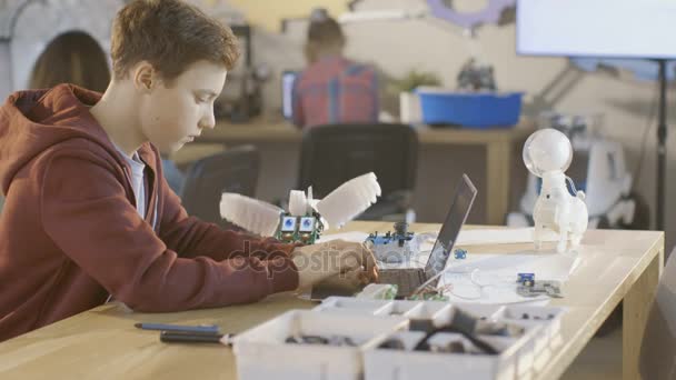 O menino esperto trabalha em um portátil para seu projeto novo da programação do robô na classe da ciência da computação. Outras crianças aprendendo em segundo plano . — Vídeo de Stock