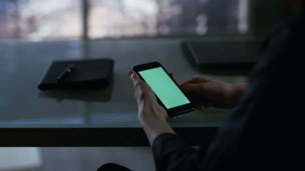 Au-dessus de l'épaule Vue de Businesswoman assis à son bureau et en utilisant Smartphone avec écran vert. La grande ville est vue par la fenêtre .