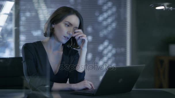 Kvinnliga verkställande arbetar på en bärbar dator i sitt privata kontor med utsikt över stora staden. Hon är problemlösning och är omtänksam. Hennes arbetsytan görs i mörka övertoner, med nakna Cement väggar. — Stockvideo