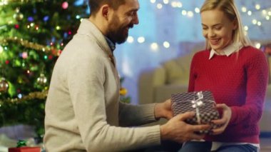 Yakışıklı adam onun güzel kız arkadaşı için Noel hediyesi veriyor. Parlak oda ile süslenmiş Noel ağacı içinde belgili tanımlık geçmiş bulunmaktadır.