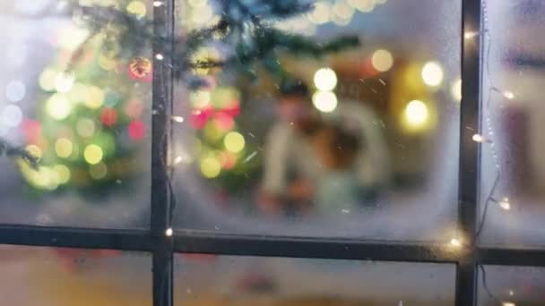 Looking Through Snowy Window. Sitting Under Christmas Three with Gifts Under It Father Uses Tablet Computer with His Daughter. — Stock Video