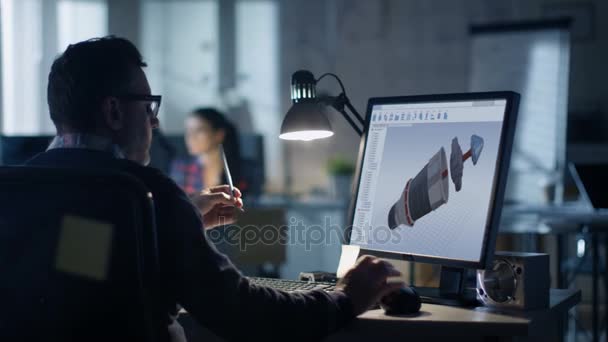 事務所で夜遅く。設計エンジニアは、自分のパソコンで動作します。彼の展示は、設計図を参照してください。オフィスは近代的に見えます。背景の方々 の. — ストック動画