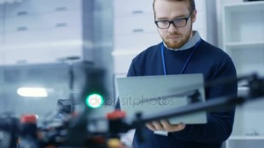 Genç erkek mühendis programları dron O'nun elinde tutan Laptop süre. O parlak Modern teknoloji laboratuarında çalışıyor.