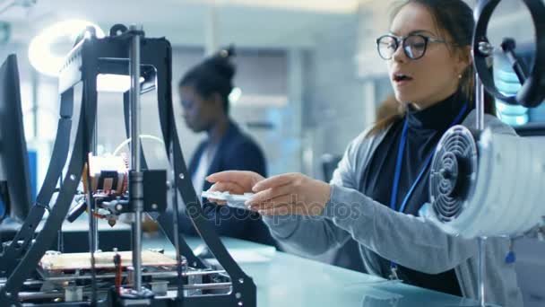 Die junge schöne Wissenschaftlerin schafft mit einem 3D-Drucker Details und installiert sie auf ihrem Prototypen. sie arbeitet in einem modernen Labor. — Stockvideo