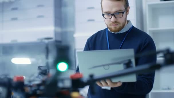 Jonge mannelijke ingenieur programma's Drone terwijl Holding Laptop in zijn handen. Hij werkt in een lichte moderne High-Tech-laboratorium. — Stockvideo