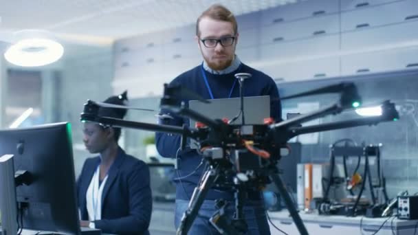 Stilig Man och African American Woman ingenjörer arbetar med ett Drone projekt med hjälp av Laptop och ta anteckningar. Han arbetar i ljusa moderna högteknologiska laboratorium. — Stockvideo
