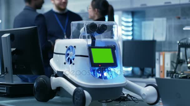 Groupe multiethnique de jeunes scientifiques et de scientifiques brillants, hommes et femmes, discutent amicalement dans l'atmosphère informelle. Le grand laboratoire moderne / centre de recherche a le robot avec l'écran vert de maquette .