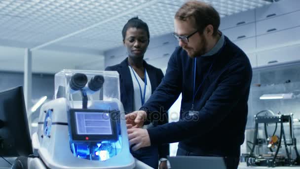 Ingenieros masculinos blancos y femeninos negros trabajando conjuntamente en un proyecto de robótica. Están en un laboratorio moderno. . — Vídeos de Stock