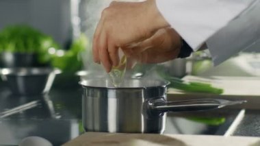 Şef kaynama çanak içine bir yumurta kırıldığında bir ocakta tencerede close-up. Paslanmaz Çelik Mutfak Modern görünüyor.