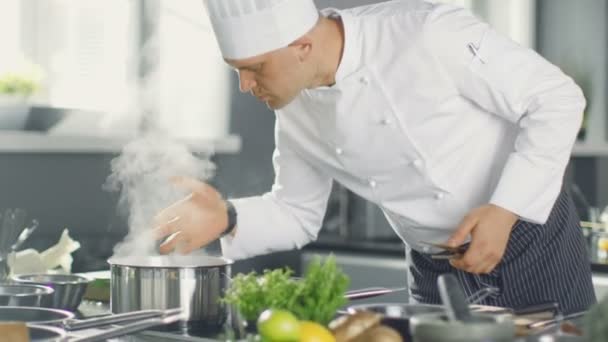 Slavný šéfkuchař restaurace voní páru z hrnce. Jeho příprava jídla v moderní kuchyni.