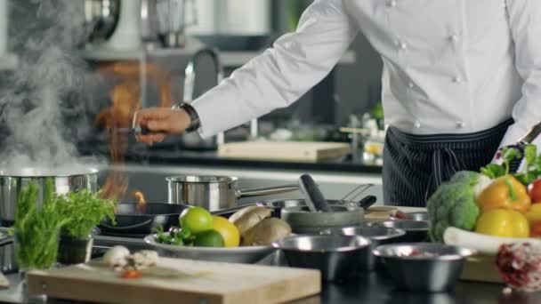 Chef professionnel allume l'huile sur une casserole. Cuisine de style flambe. Il travaille dans une cuisine moderne avec beaucoup d'ingrédients couchés autour . — Video