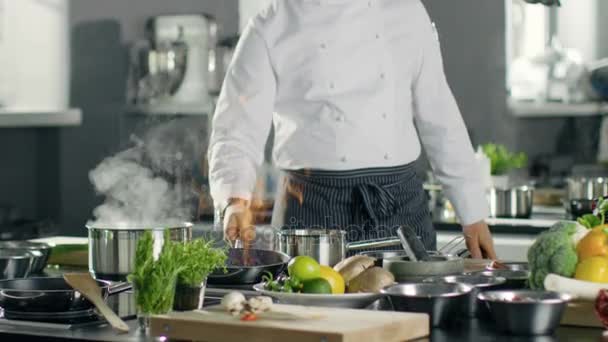 Chef profesional enciende aceite en una sartén. Cocina estilo Flambe. Trabaja en una cocina moderna con muchos ingredientes por ahí. . — Vídeo de stock