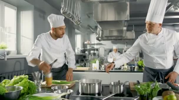 Two Famous Chefs Work as a Team in a Big Restaurant Kitchen. Vegetables and Ingredients are Everywhrere, Kitchen Looks Modern with Lots of Stainless Steel. — Stock Video