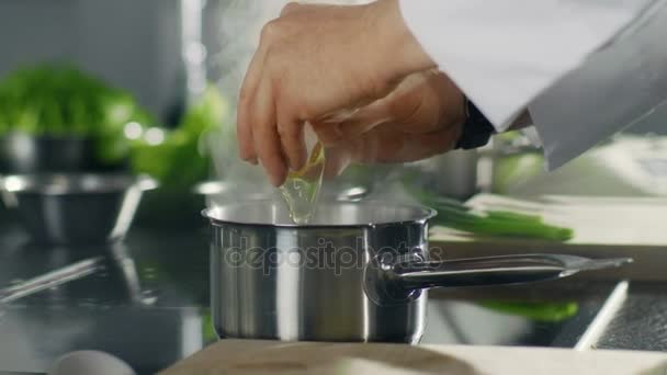 Detail z hrnce na vařič, když kuchař vejce do varné misky. Nerezové kuchyňské vypadá moderní.