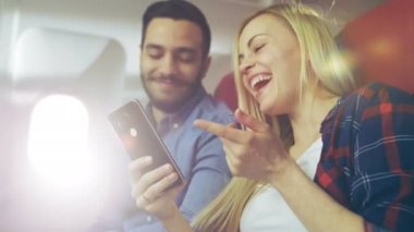 Ticari uçak bir gemide güzel genç sarışın yakışıklı İspanyol erkek ile kullanma Smartphone ve gülmek. Uçak pencereden güneş parlıyor.