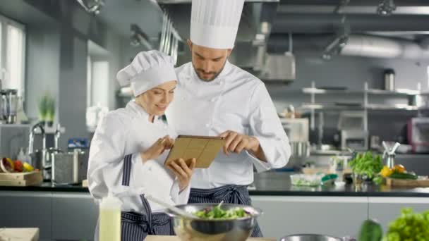 Chefs célèbres masculins et féminins discutent de leur blog vidéo tout en utilisant Tablet Computer. Ils travaillent sur une grande cuisine professionnelle en acier inoxydable de restaurant . — Video