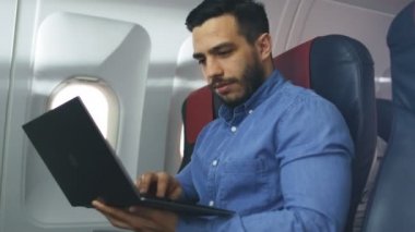 Ticari uçak yakışıklı İspanyol erkek işleri onun laptopunda bir gemide. Uçak pencereden güneş parlıyor.