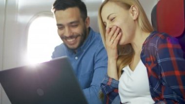 Ticari uçak bir gemide güzel genç sarışın yakışıklı İspanyol erkek ile bir dizüstü bilgisayar ve gülmek film izlemek. Uçak pencereden güneş parlıyor.