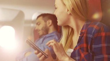 Yönetim Kurulu, ticari uçak güzel genç sarışın kullanır smartphone cep telefonu ile onun İspanyol ise erkek komşu uyur. Uçak pencereden güneş parlıyor.