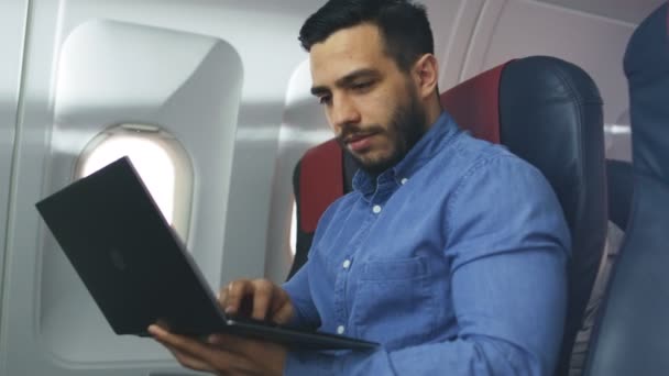 En una Junta de Aviones Comerciales el apuesto Hombre Hispano trabaja en su computadora portátil. Sol brilla a través de la ventana del avión . — Vídeos de Stock