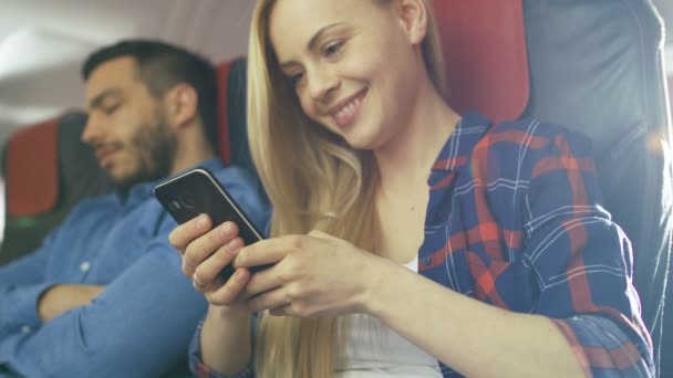 A bordo de avión comercial hermosa rubia joven utiliza Smartphone mientras que su vecino masculino hispano duerme . — Vídeos de Stock